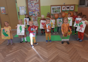 Dzieci pozują do zdjęć trzymając obrazki przedstawiające warzywa